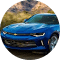 Blue modern SUV driving on a highway with wooded hills in the background.