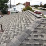 View of a shingled house roof with surrounding residential area and overcast sky.