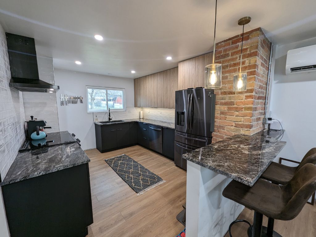 Modern kitchen with black appliances, marble counters, and a brick pillar.